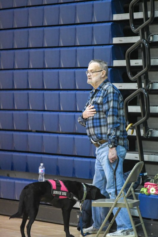 A Sussex Central wrestling fan with a service dog stands for the national anthem.